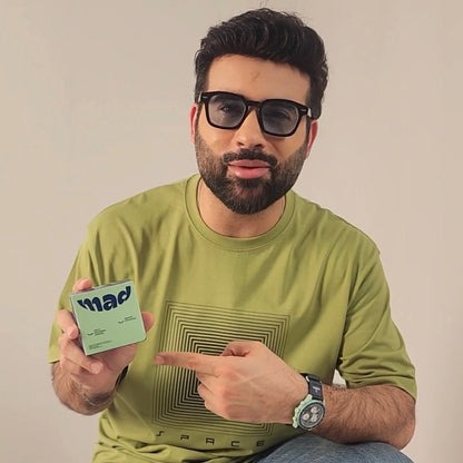 Man wearing glasses and a green shirt holding a product with a brand logo. Mad Care Teeth Whitening Powder 
