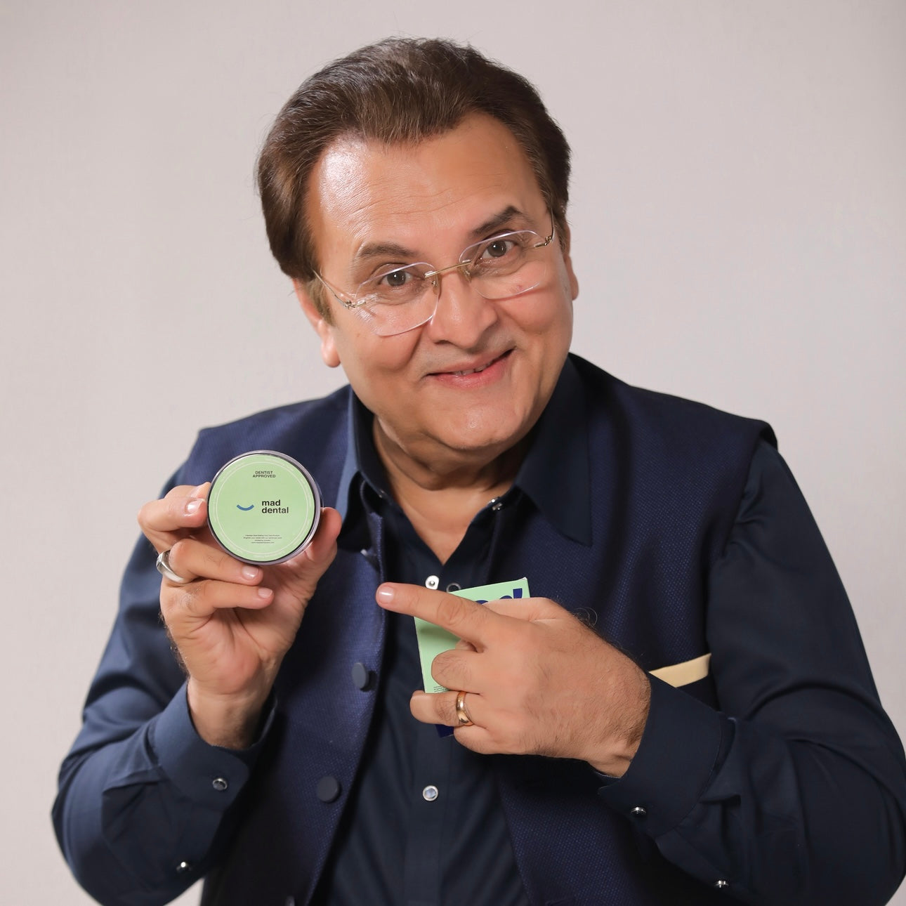 Man holding a small green container and a card against a plain background. Mad Care Teeth Whitening Powder 