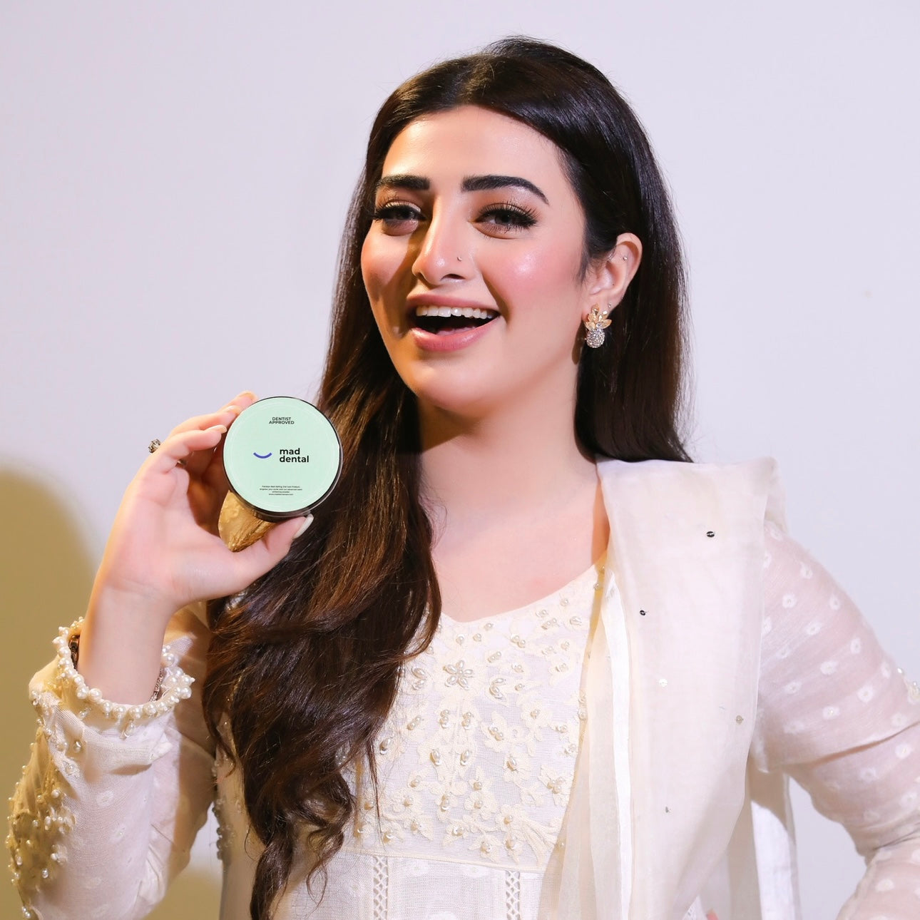 Woman holding a product container with a plain background. Mad Care Teeth Whitening Powder 