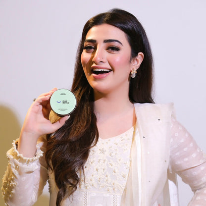 Woman holding a product container with a plain background. Mad Care Teeth Whitening Powder 